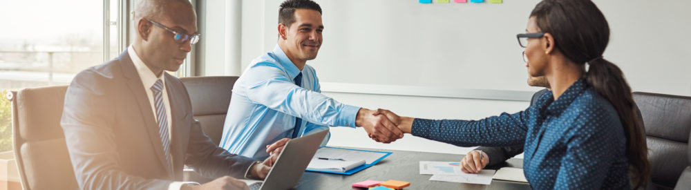 Two business colleagues shaking hands across the table in congratulations during a multiracial business meeting at a conference table in the office